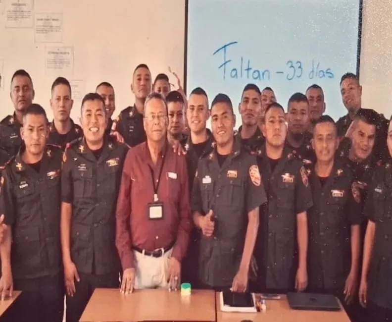 Captain Zepeda, in a wine-colored shirt, at the center of a large group of sergeants in a classroom; the blackboard reads «33 days left»