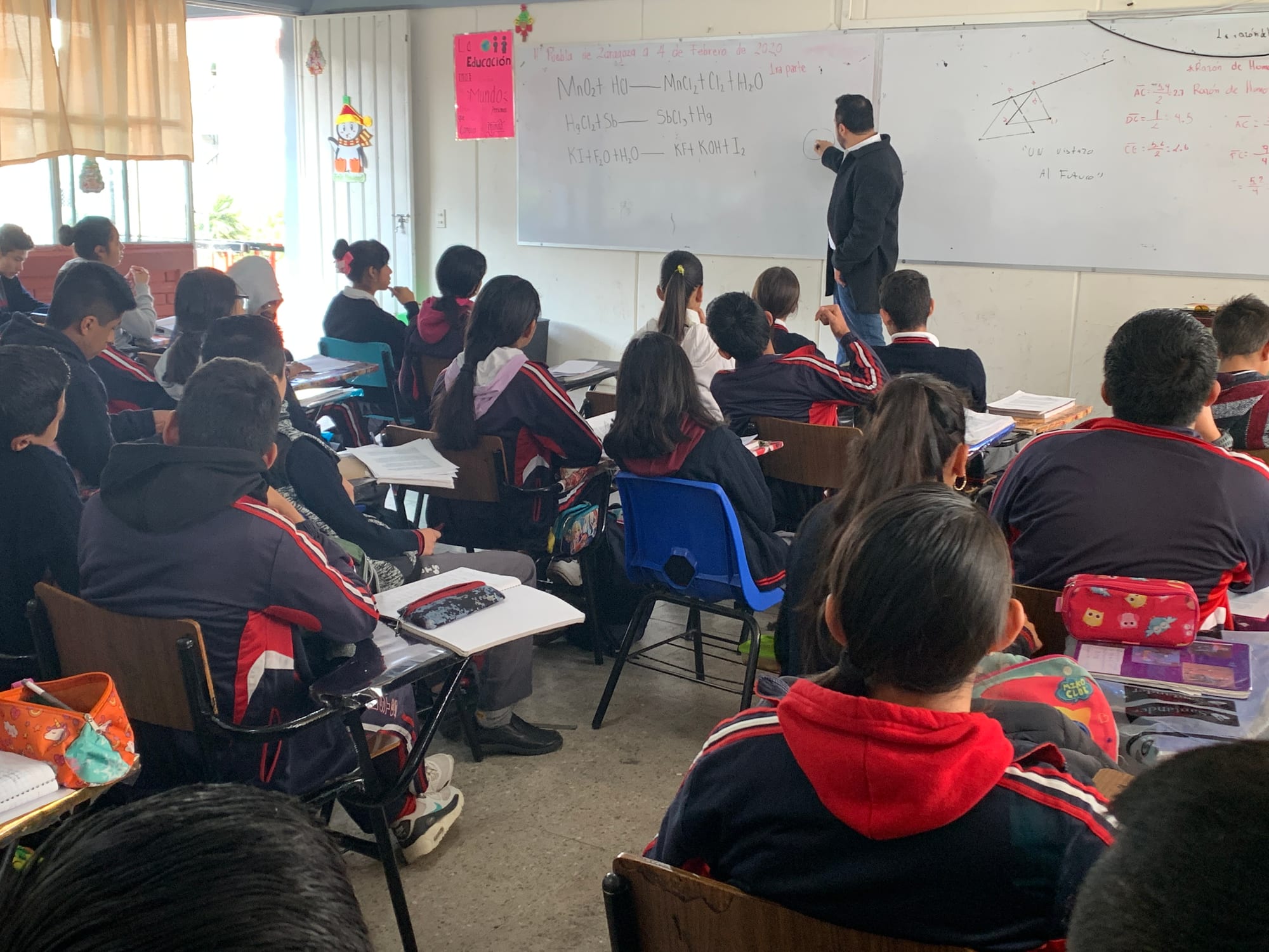 Arturo Ordorika escribe en el pizarrón de un salón en Puebla, con el grupo de espaldas