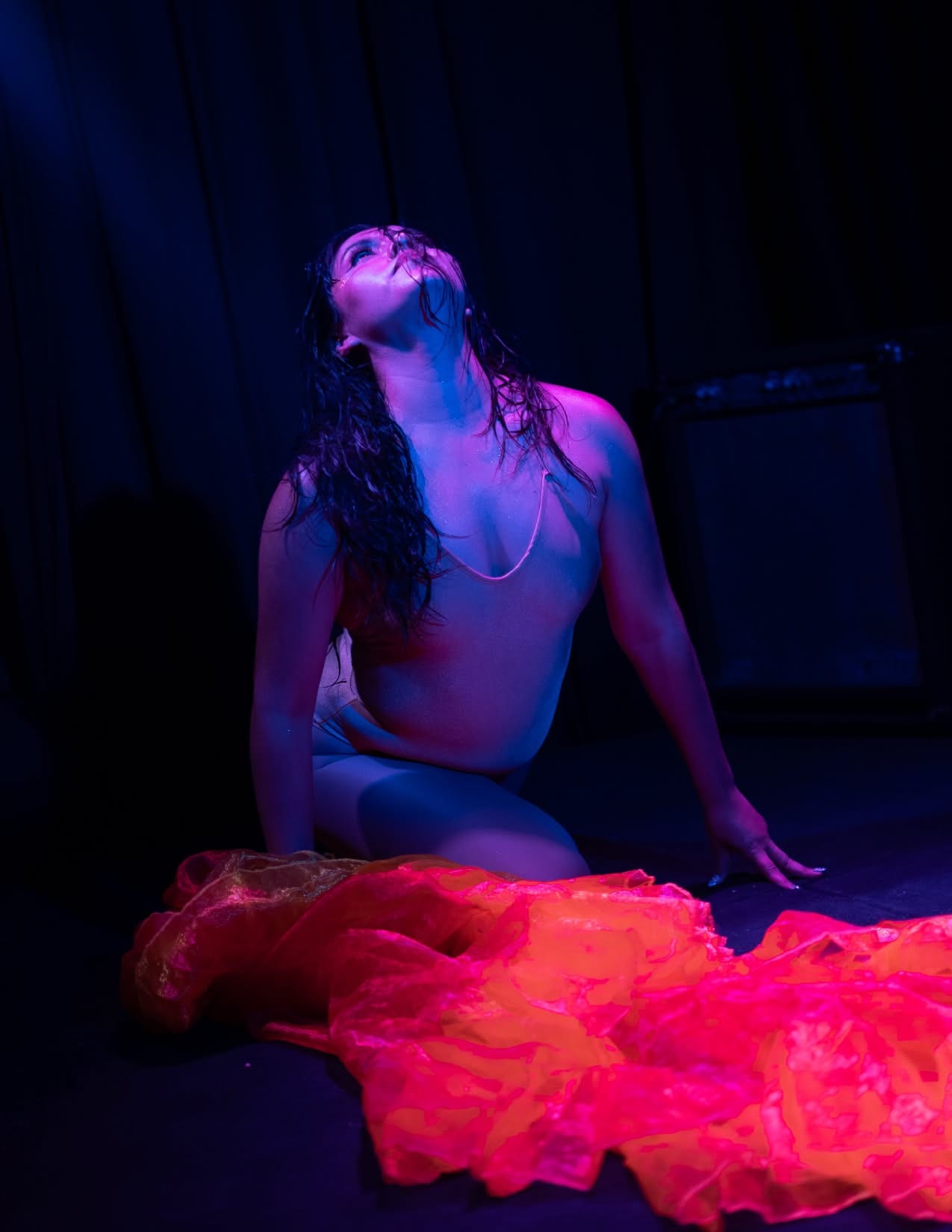 Ángeles Rodríguez en el suelo, la cabeza hacia la luz, el velo rojo extendido, bajo luz azul y rosa, en el estreno de Sirena Interior
