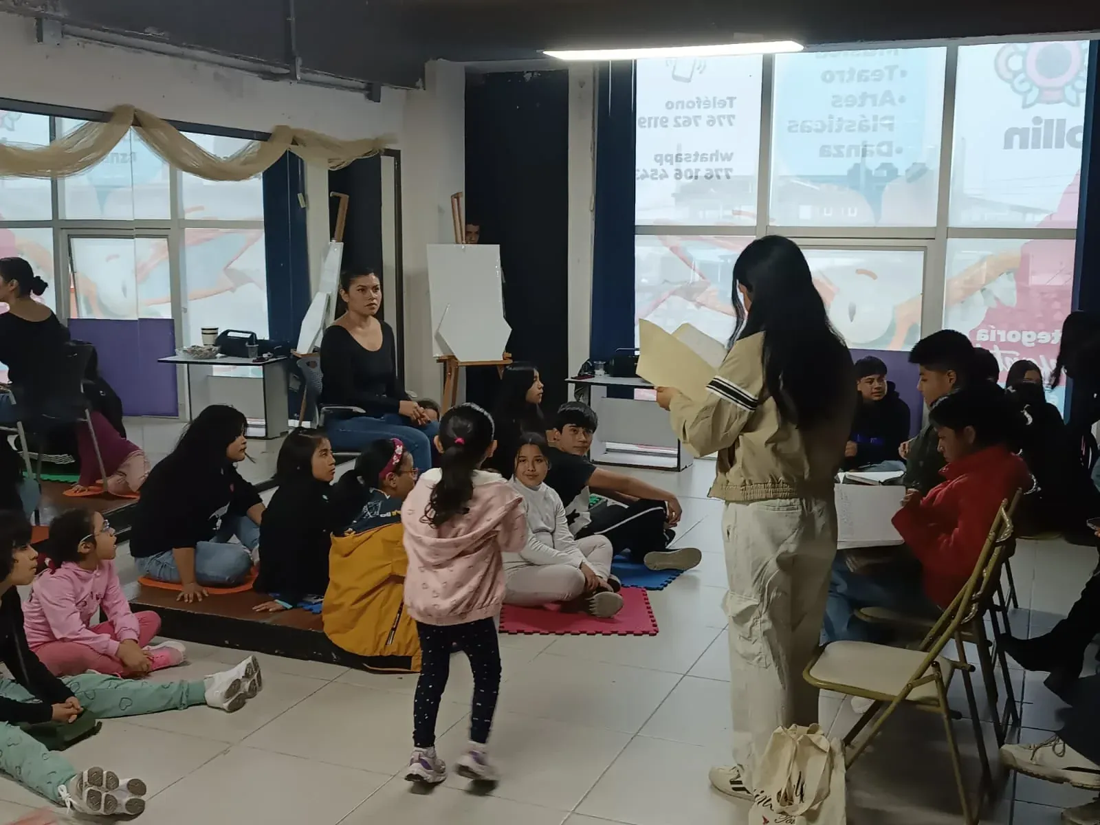 A class at Ollin: girls and boys sitting on the floor of the hall of mirrors listen to a student reading aloud